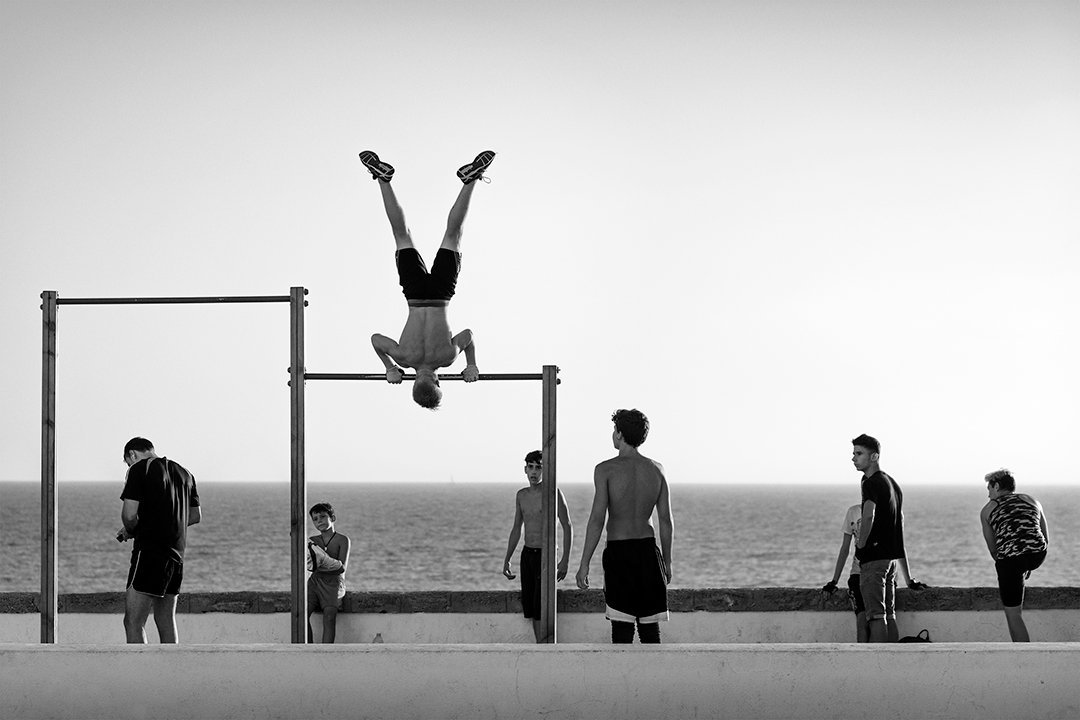 A person upside down on exercise bars facing the sea.